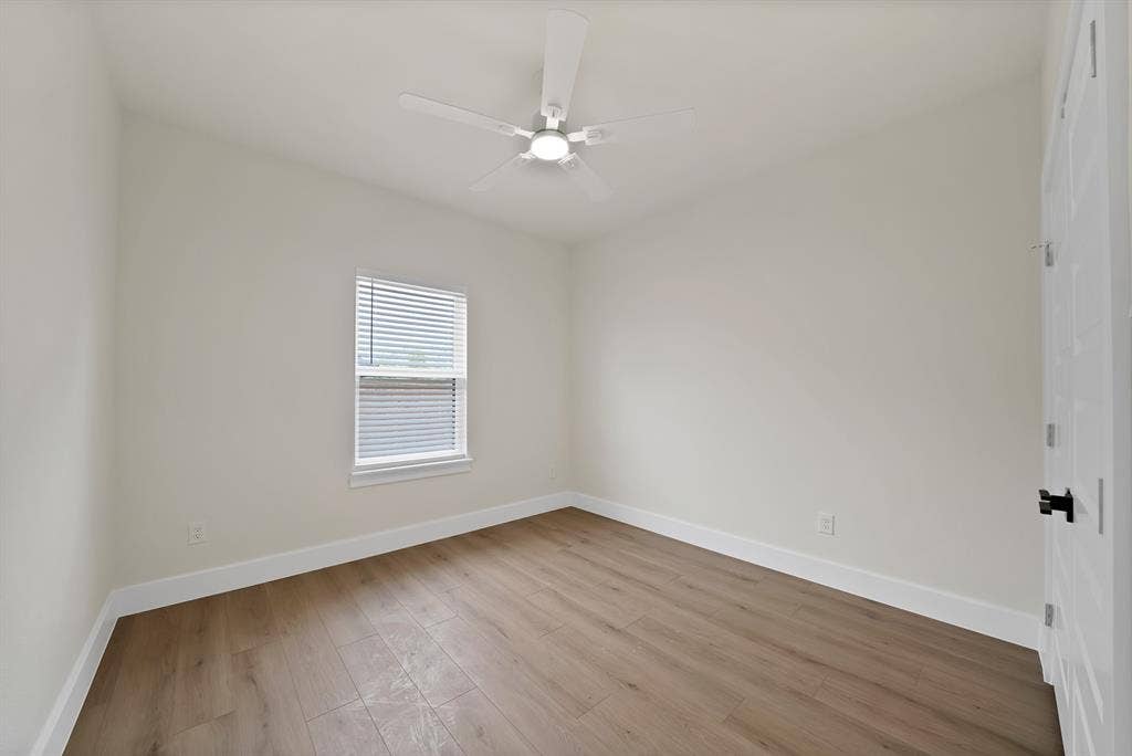 Interior room featuring wood-finish flooring, a neutral color palette, a central ceiling fan with integrated lighting, and a single-hung window with blinds
