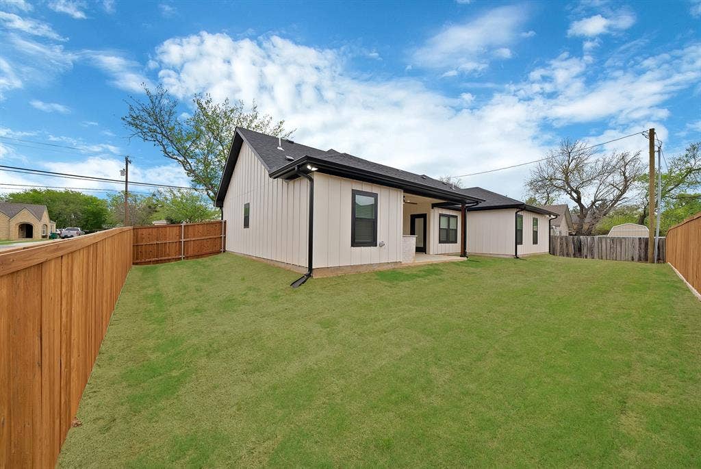 Rear exterior featuring vertical board-and-batten siding, a covered patio, dark window frames, and an enclosed fenced yard