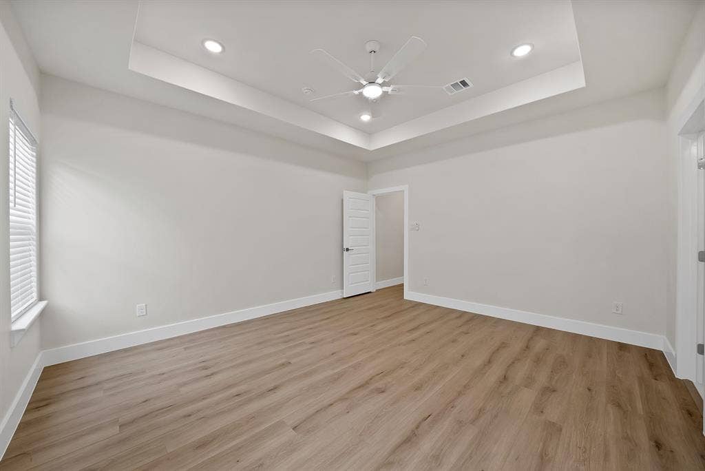 Tray ceiling with recessed lighting, wood-finish flooring, and a white ceiling fan