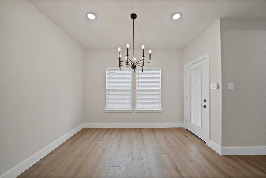 Room featuring wood-finish flooring, recessed lighting, a multi-arm candle-style chandelier, dual windows with integrated blinds, and a paneled entry door