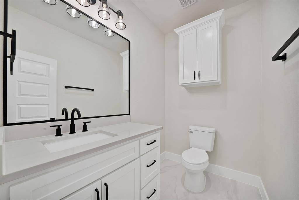 Bathroom featuring a white vanity with a quartz countertop, an integrated rectangular sink, black matte hardware, a wall-mounted storage cabinet, and an oversized framed mirror