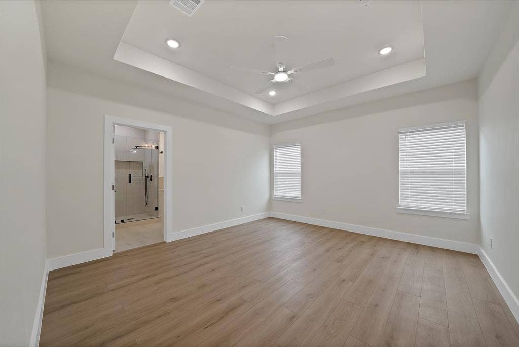 Room featuring a tray ceiling, wood-finish flooring, recessed lighting, and a ceiling fan with an integrated light fixture
