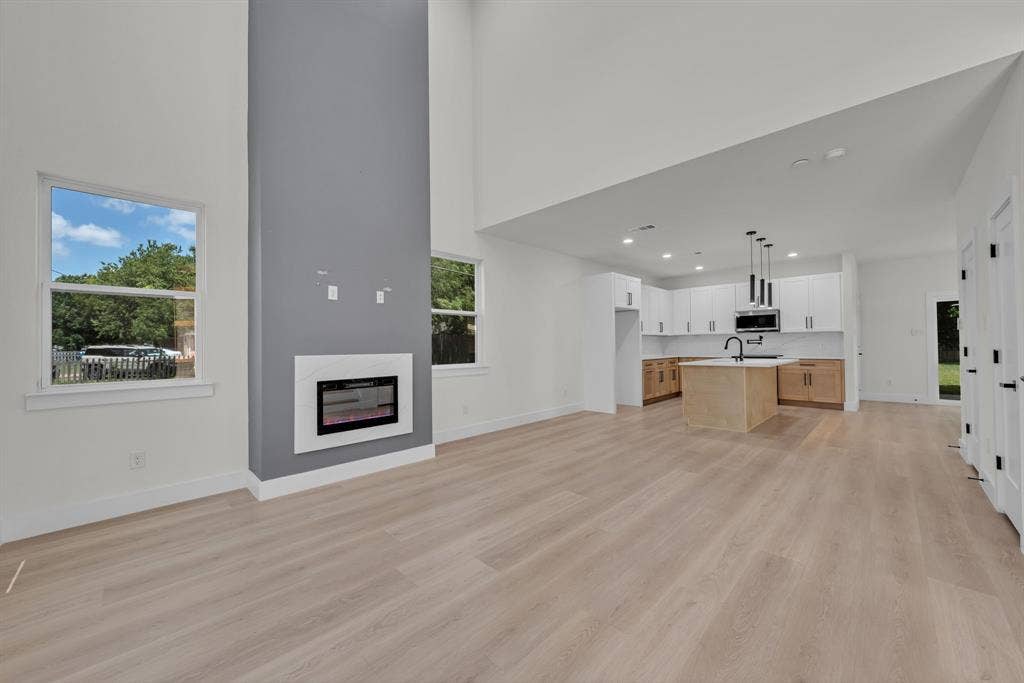 3639 Pueblo Street, Dallas, TX 75212 High-ceiling living area featuring wood-finish flooring, a full-height gray accent wall, and a built-in fireplace with a white surround