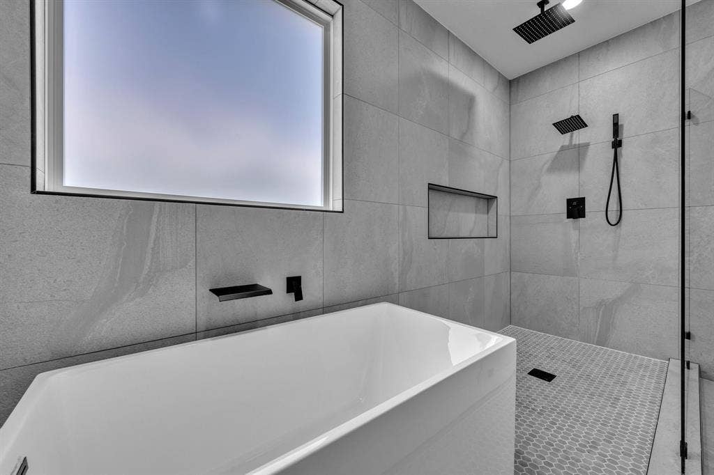 3639 Pueblo Street, Dallas, TX 75212 Freestanding soaking tub with matte black wall-mounted faucet, walk-in shower featuring large-format tile walls, ceiling-mounted rainfall showerhead, handheld shower fixture, and built-in wall niche
