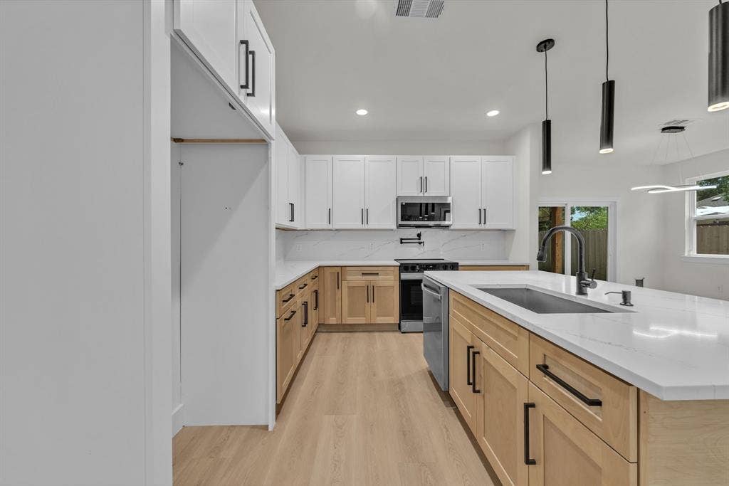 3639 Pueblo Street, Dallas, TX 75212 Kitchen featuring two-tone cabinetry with matte black hardware, quartz countertops, a central island with an undermount stainless steel sink, wood-finish flooring, and minimalist pendant lighting