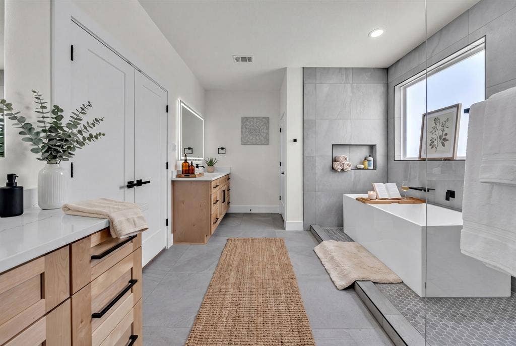 3639 Pueblo Street, Dallas, TX 75212 Bathroom featuring light wood-finish cabinetry, white solid-surface countertops, large-format tile flooring, a freestanding rectangular soaking tub, and a glass-enclosed shower area with a built-in recessed wall niche