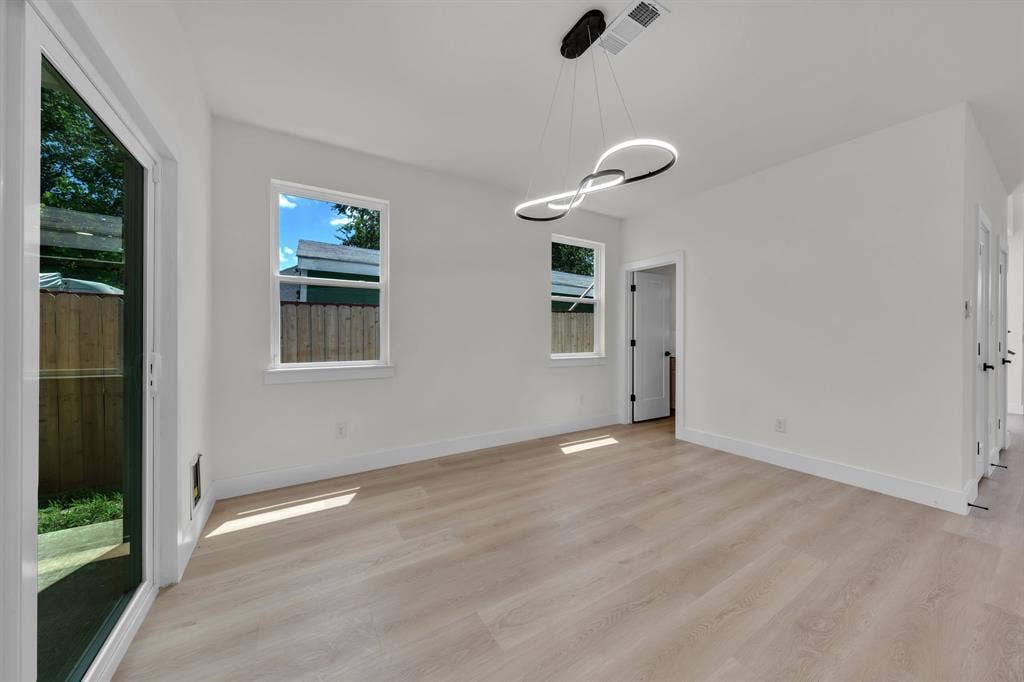 3639 Pueblo Street, Dallas, TX 75212 Light-filled room featuring wood-finish flooring, white walls, double-pane windows, a sliding glass door, and a modern circular LED pendant light fixture