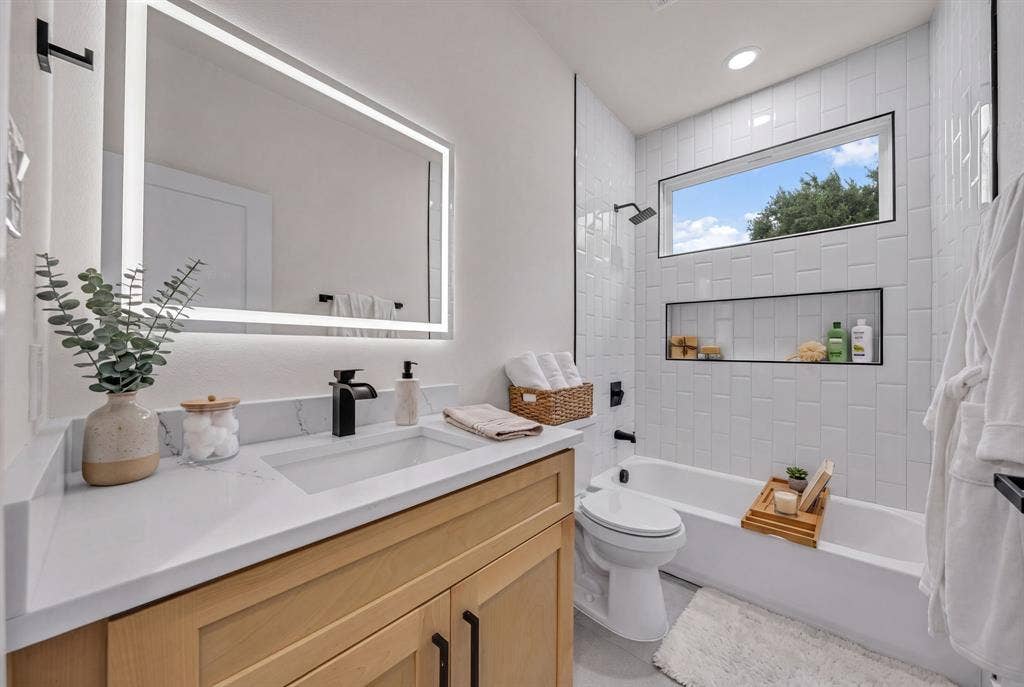 3639 Pueblo Street, Dallas, TX 75212 Light-toned wood vanity with a white countertop, rectangular undermount sink, matte black faucet, and rectangular LED-backlit mirror