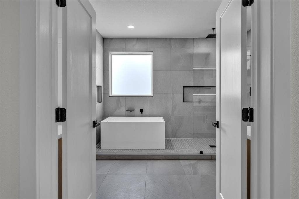 3639 Pueblo Street, Dallas, TX 75212 Freestanding soaking tub, walk-in shower with glass enclosure, floor-to-ceiling large-format wall tile, built-in recessed wall niches, and matte black fixtures