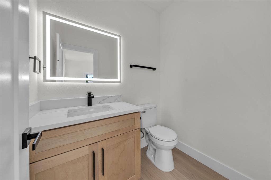 3639 Pueblo Street, Dallas, TX 75212 Wood-finish vanity with a rectangular sink, white countertop, matte black faucet, and rectangular LED-backlit mirror