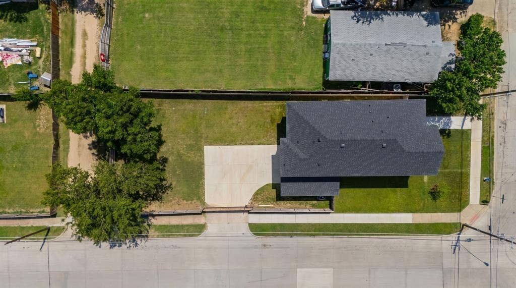 3639 Pueblo Street, Dallas, TX 75212 Aerial perspective of a corner lot featuring a concrete driveway, mature trees, expansive lawn space, and a dark-toned asphalt shingle roof