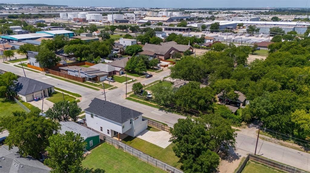 3639 Pueblo Street, Dallas, TX 75212 Aerial view of a multi-level residence featuring a dark shingle roof, white exterior siding, concrete driveway, and a wood privacy fence