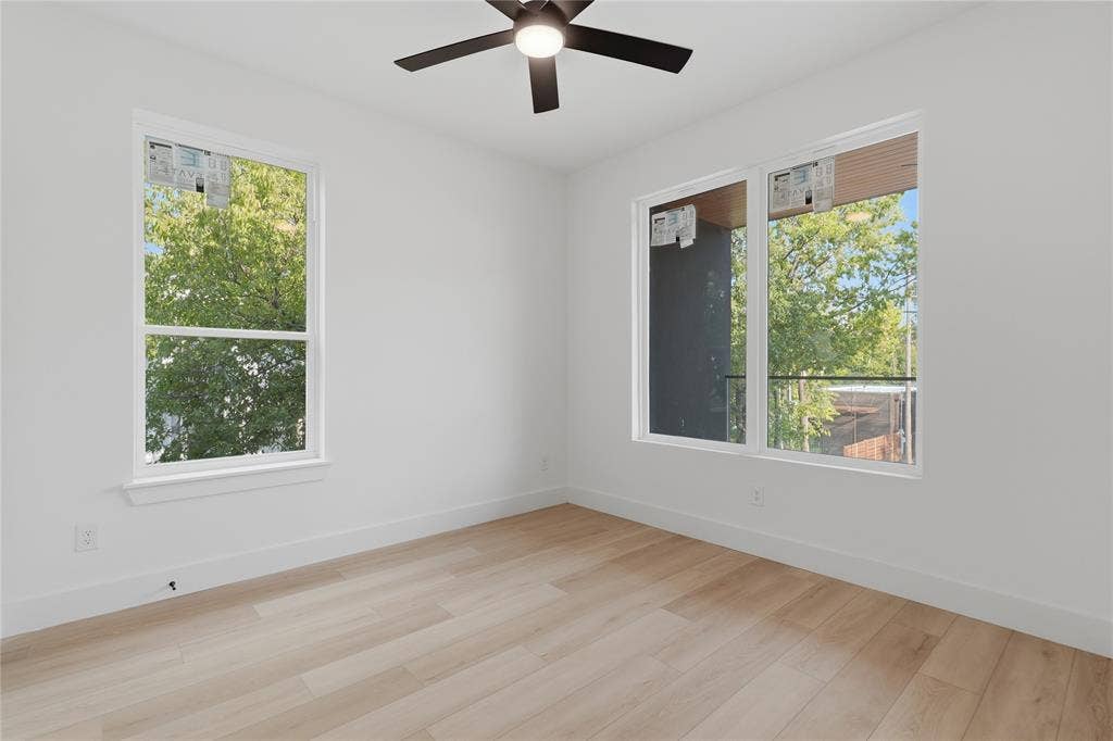 Room featuring light wood-finish flooring, dual-pane windows, and a ceiling-mounted light fixture with fan blades