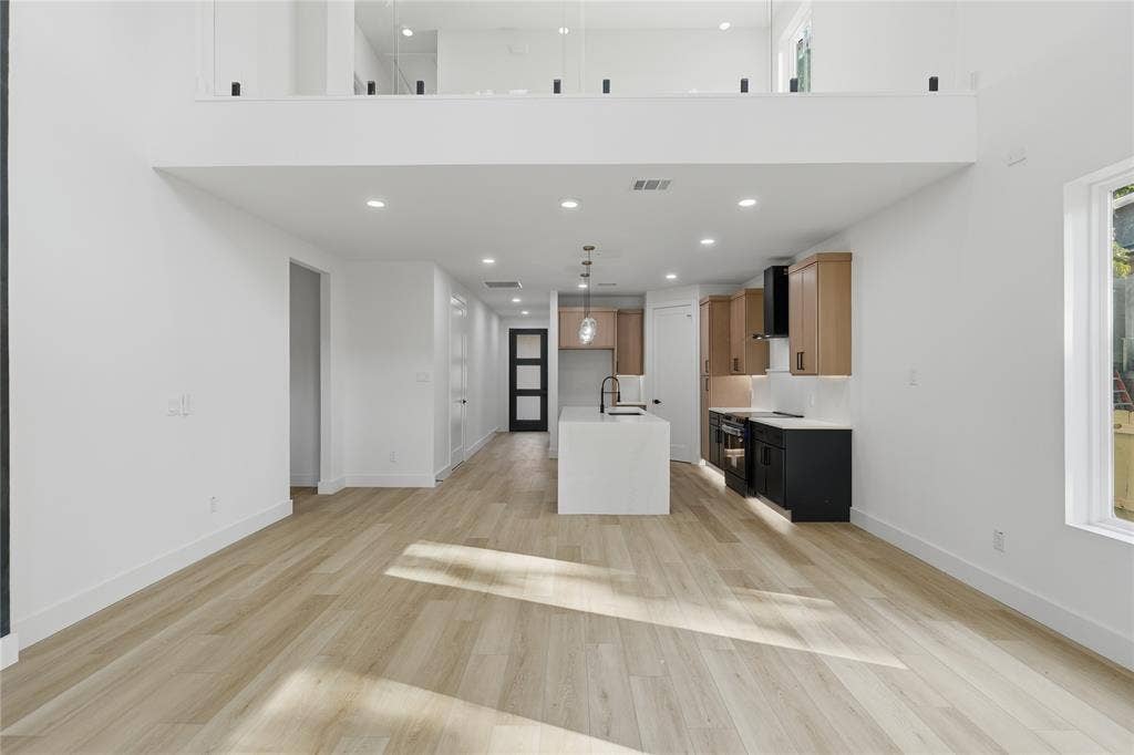 Open-concept interior featuring wood-finish flooring, a kitchen island with a quartz countertop, dual-tone cabinetry, recessed lighting, and a glass-paneled mezzanine railing