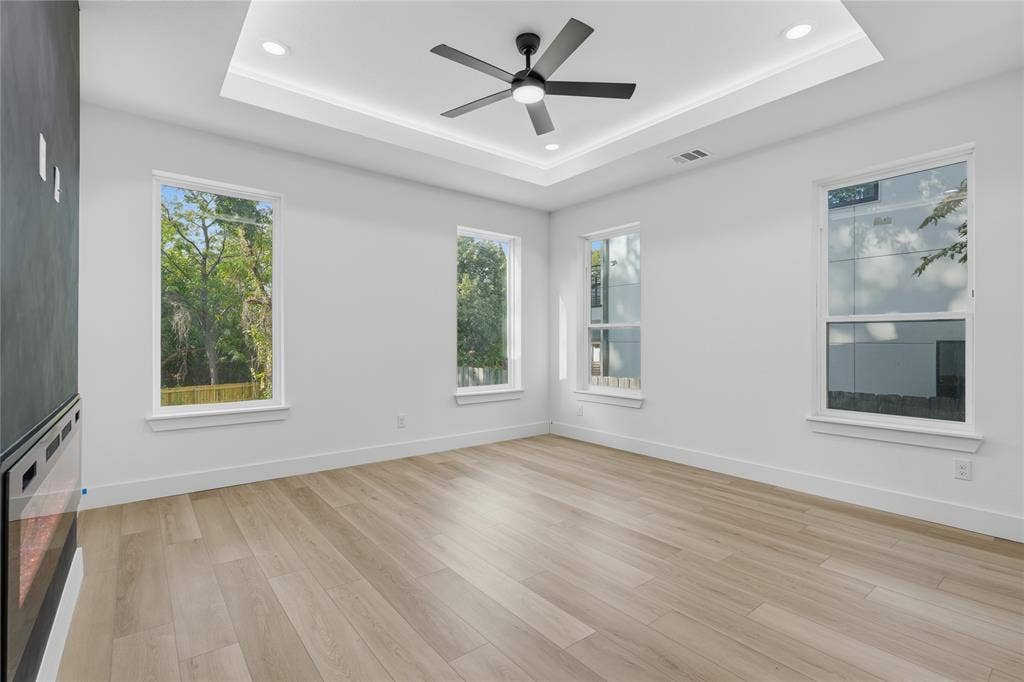 Tray ceiling featuring recessed lighting, wood-finish flooring, wall-mounted electric fireplace with a dark surround, and multiple energy-efficient windows