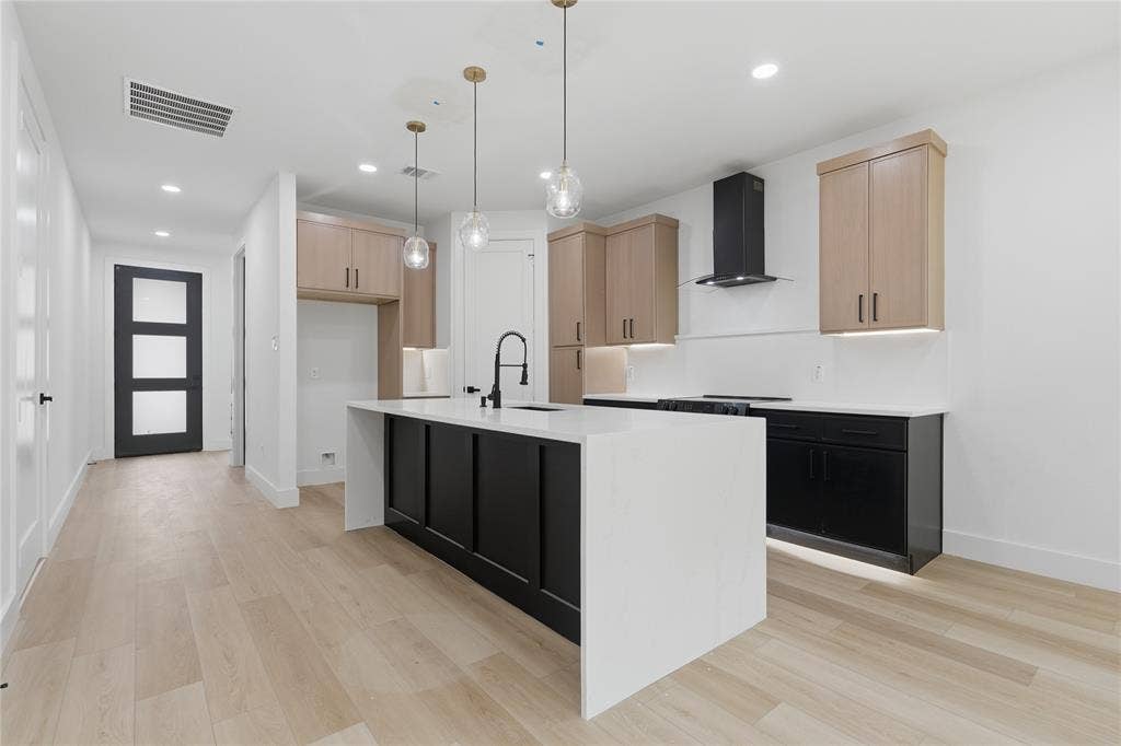 Kitchen featuring two-tone cabinetry, central island with waterfall-edge countertop, matte black faucet, and pendant lighting