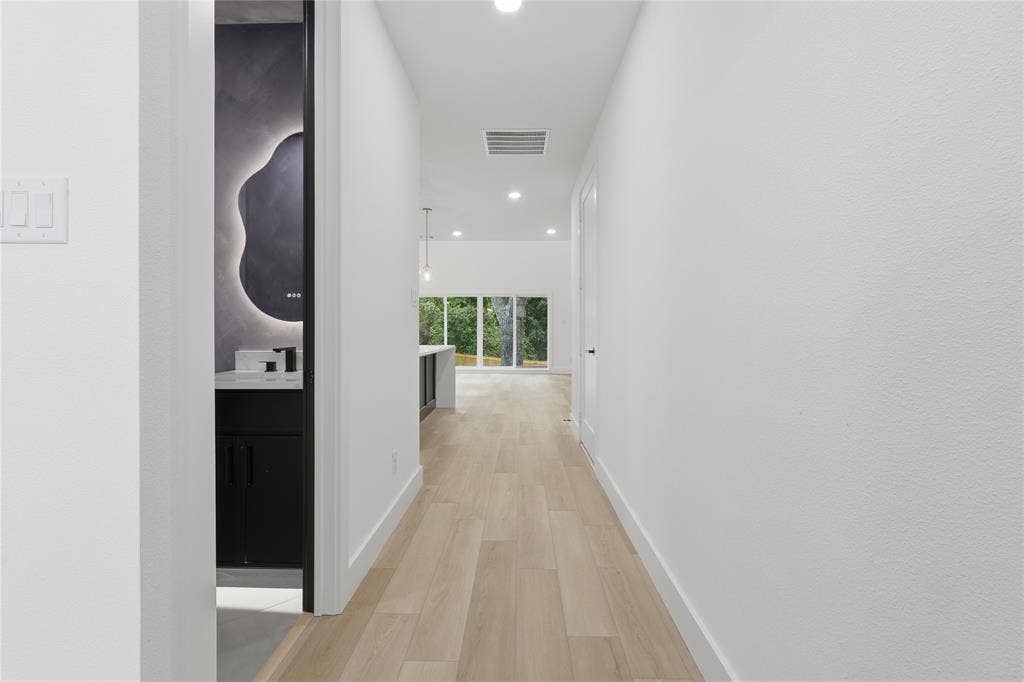 Hallway featuring wood-finish flooring, recessed lighting, and a dark-toned vanity with an illuminated mirror