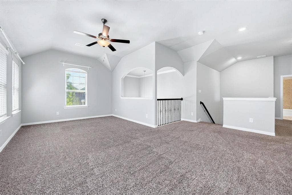 Vaulted ceilings with recessed lighting, wall-to-wall carpeting, archway architectural detailing, metal spindle railing, and a ceiling fan