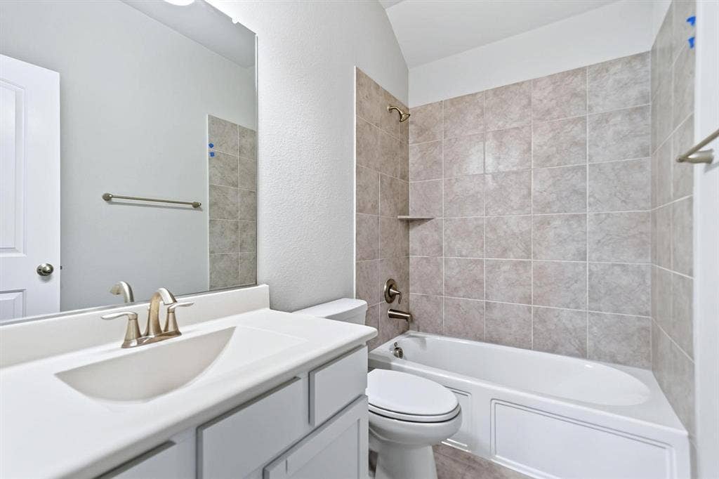 Bathroom featuring a white vanity with integrated sink, brushed-nickel faucet, large wall-mounted mirror, and tub-shower combination with ceramic tile surround
