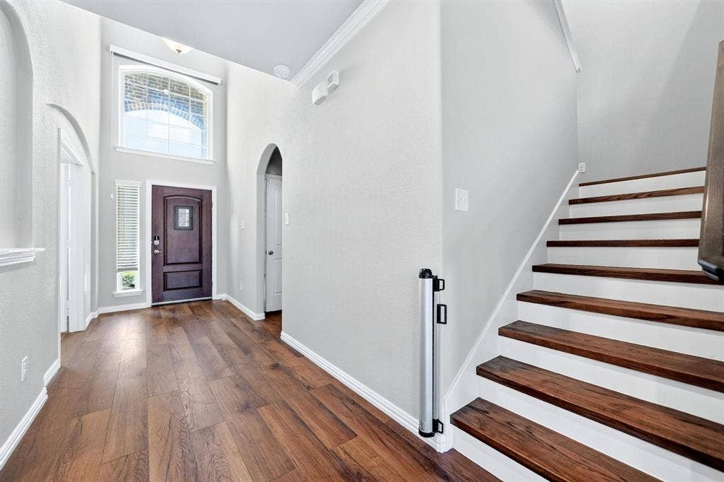 Foyer featuring high ceilings, wood-finish flooring, an arched doorway, a transom window, and a staircase with wood treads