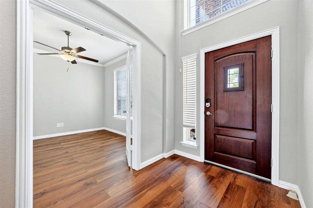 Entryway with high ceilings, wood-finish flooring, solid wood door with inset window, and double French doors opening to an auxiliary room with a ceiling fan