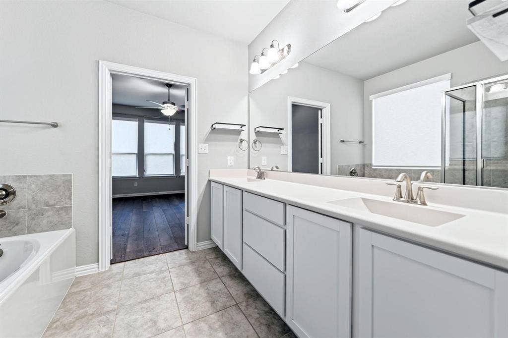 Dual-sink vanity with light-colored cabinetry and solid-surface countertop, full-width vanity mirror, tile flooring, and separate shower enclosure