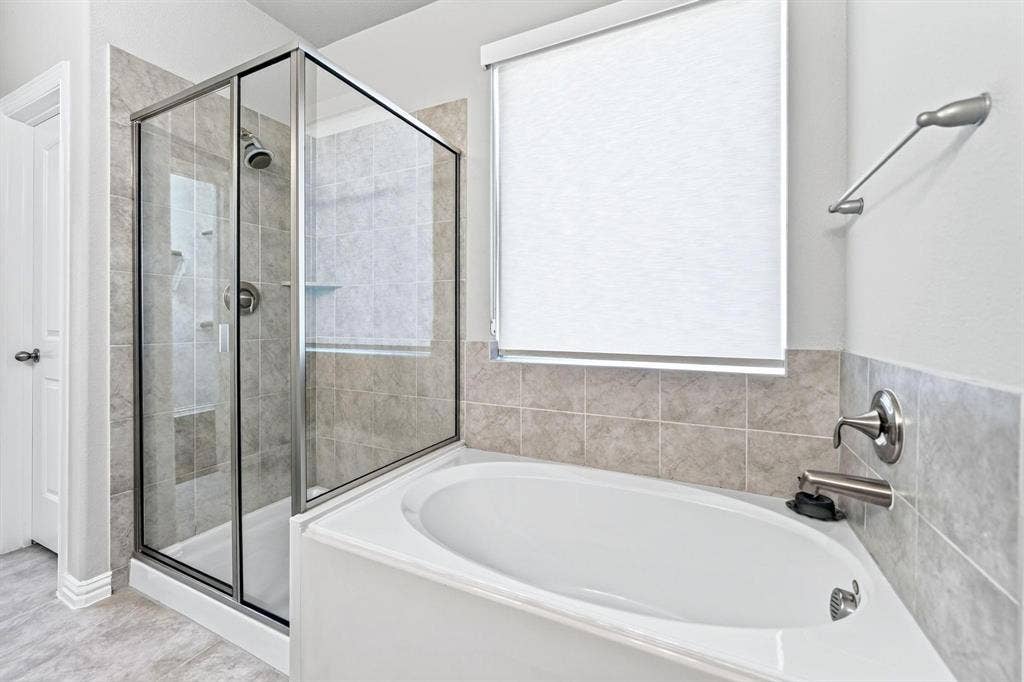 Enclosed glass shower with chrome fixtures and an oval soaking tub surrounded by neutral-toned wall tile
