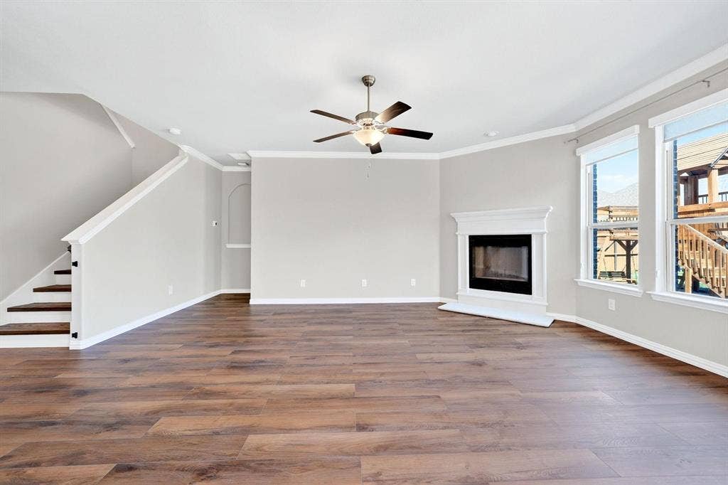 Open floor plan featuring wood-finish flooring, a fireplace with a white mantel, crown molding, and a ceiling fan