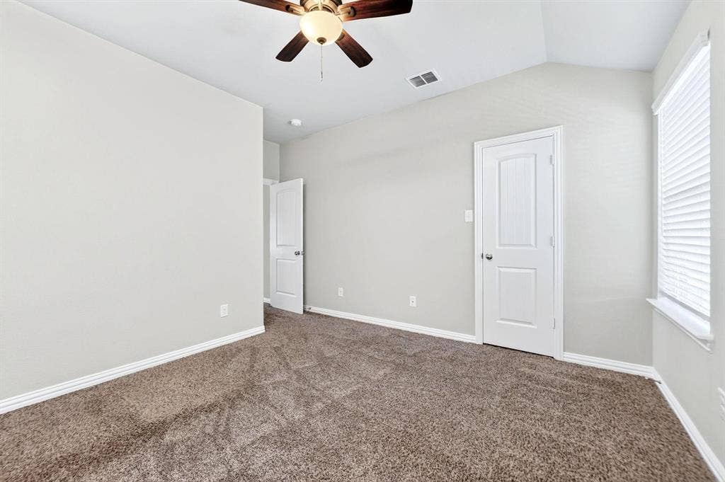 Vaulted ceiling featuring a ceiling fan with integrated lighting, neutral wall paint, carpeted flooring, and a multi-panel interior door