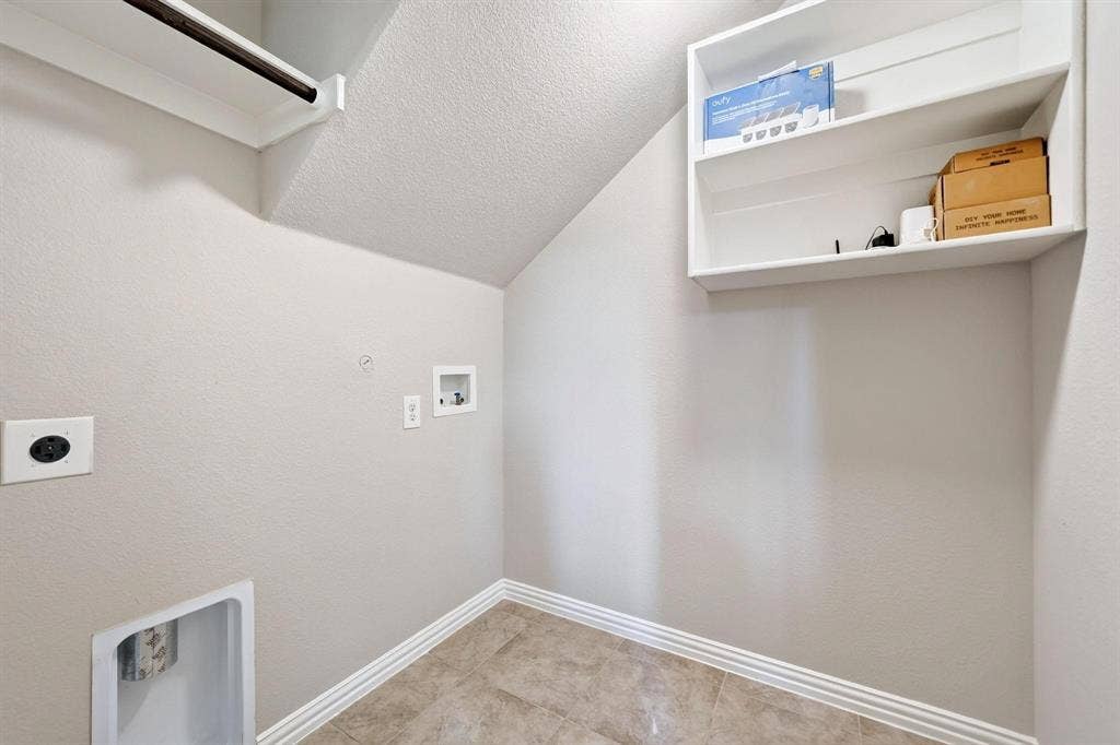 Utility space featuring ceramic tile flooring, built-in white shelving, and dedicated hookups for laundry appliances