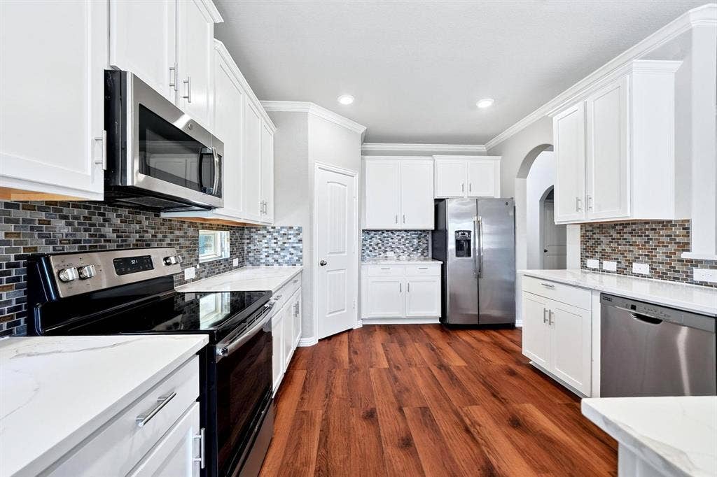 Kitchen featuring white shaker-style cabinetry, stainless steel appliances, multi-tonal mosaic tile backsplash, wood-finish flooring, and solid-surface countertops