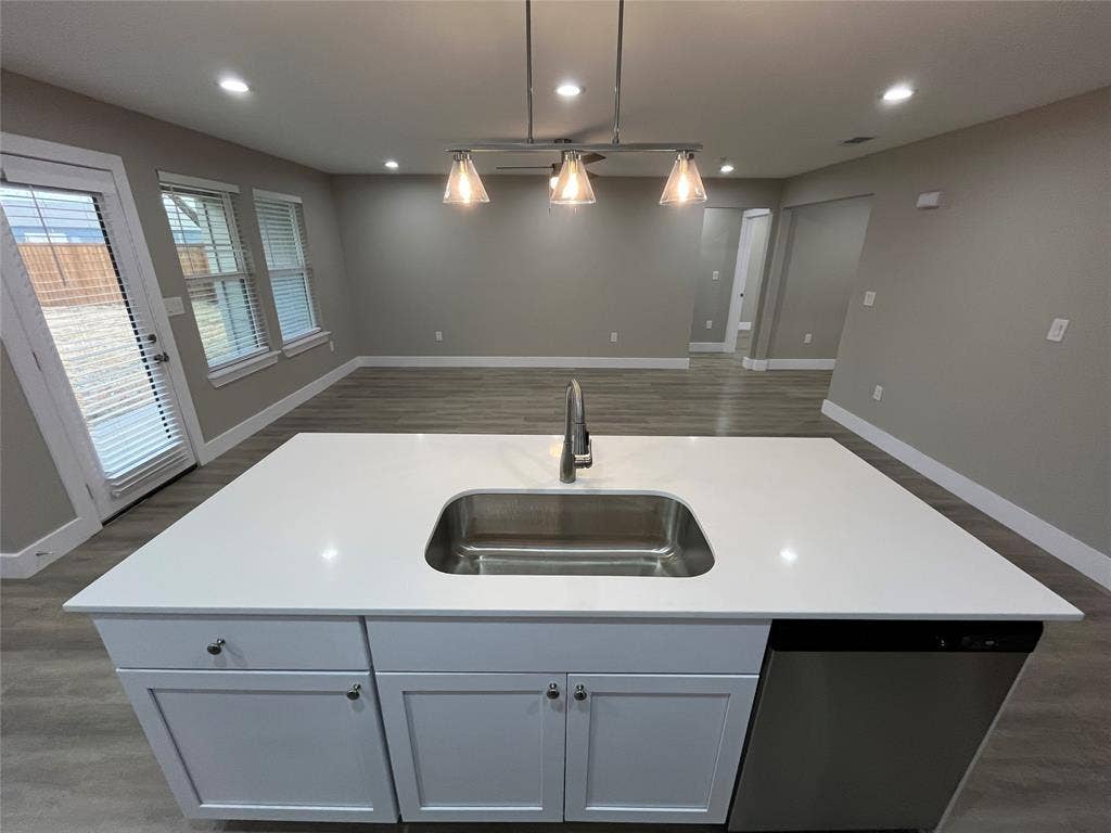 1104 Wake Drive, Richardson, TX 75081 Kitchen island featuring solid-surface countertops, an undermount stainless steel sink, wood-finish flooring, and a three-light pendant fixture
