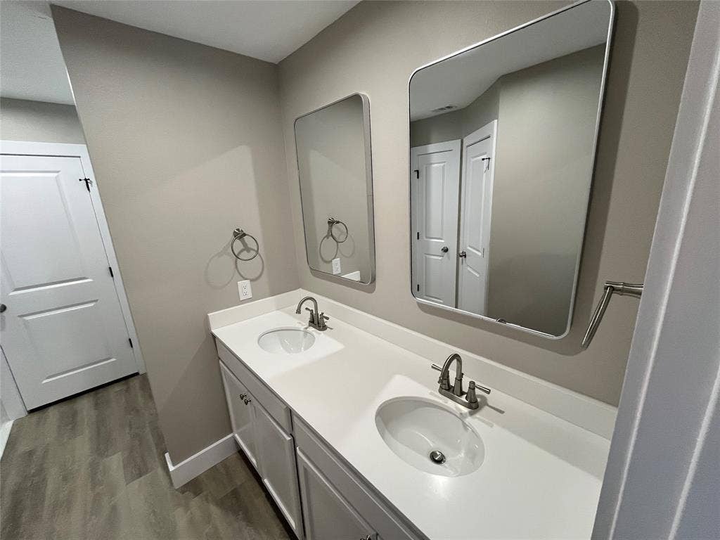 1104 Wake Drive, Richardson, TX 75081 Double vanity featuring a light-toned countertop, dual inset sinks with brushed metal faucets, soft-close cabinetry, and two rectangular wall-mounted mirrors