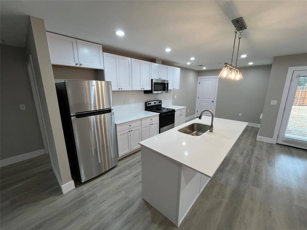 1104 Wake Drive, Richardson, TX 75081 Kitchen featuring white shaker-style cabinetry, a central island with a solid-surface countertop, stainless steel appliances, and wood-finish flooring