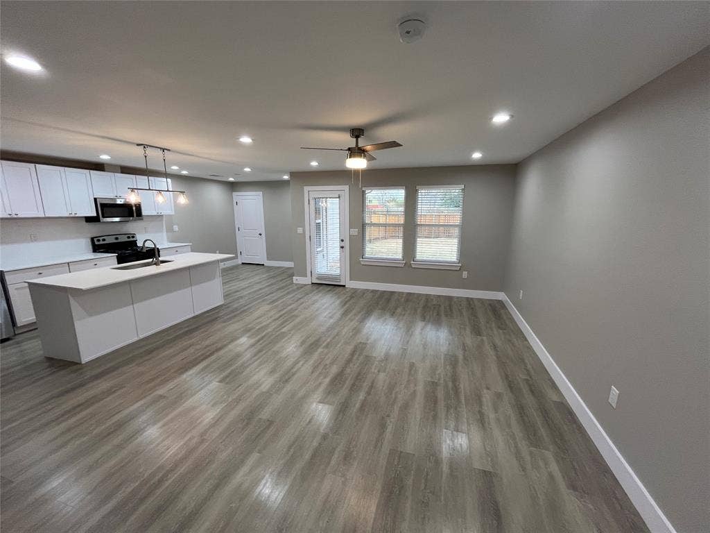 1104 Wake Drive, Richardson, TX 75081 Open concept kitchen featuring white shaker-style cabinetry, quartz countertops, a central island with an integrated sink, recessed lighting, and wood-finish flooring