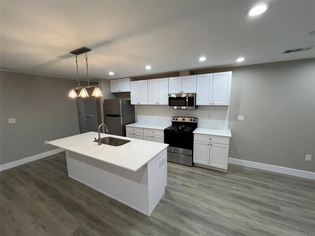 1104 Wake Drive, Richardson, TX 75081 Kitchen featuring white cabinetry, quartz countertops, a central island with an integrated stainless steel sink, recessed ceiling lighting, and wood-finish flooring