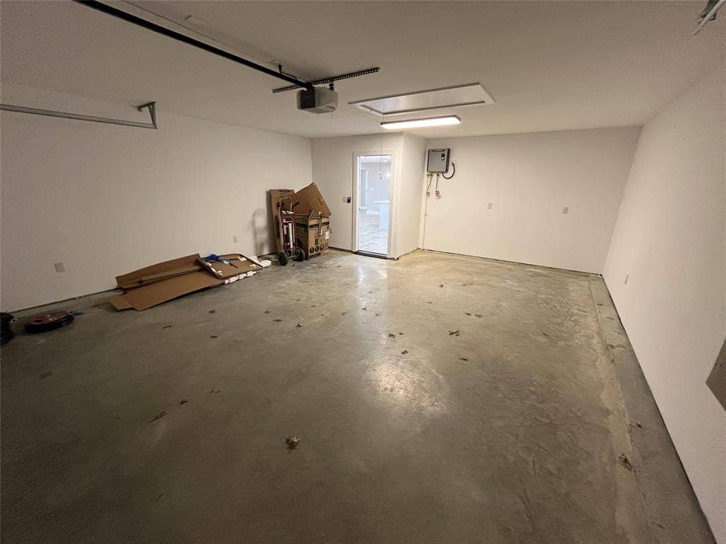 1104 Wake Drive, Richardson, TX 75081 Attached garage featuring concrete flooring, an automated overhead door opener, ceiling-mounted light fixture, and interior access point with a designated electrical panel