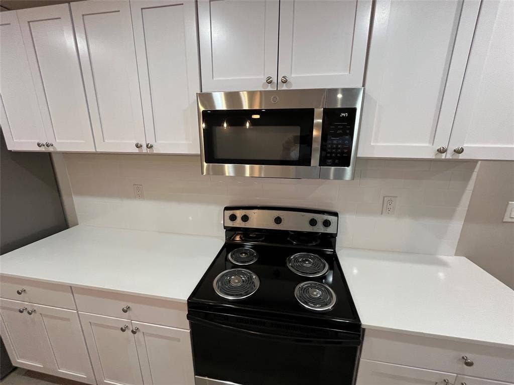 1104 Wake Drive, Richardson, TX 75081 White Shaker-style cabinetry, solid-surface countertops, subway tile backsplash, stainless steel microwave, and electric range
