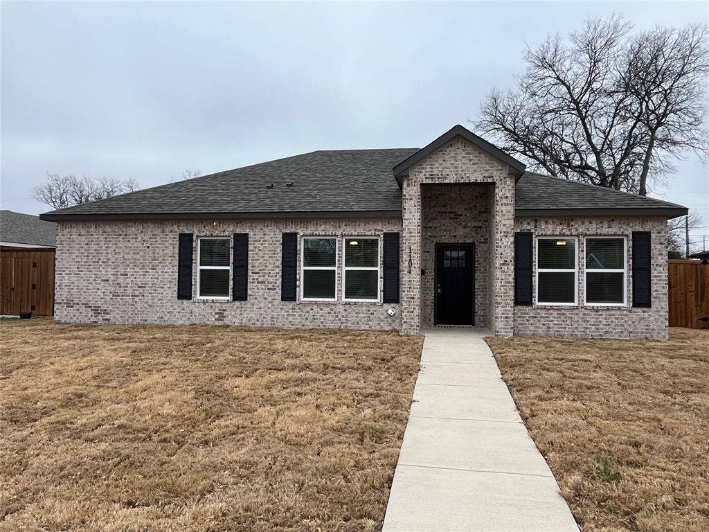 1104 Wake Drive, Richardson, TX 75081 Single-story brick exterior featuring a prominent gabled entryway, dark-toned shutters, a multi-pane glass-inlay front door, and a concrete walkway
