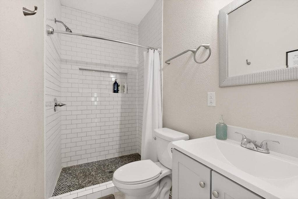 812 Centre Street, Dallas, TX 75208 Bathroom featuring white subway tile shower surround, built-in shower niche, pebble-style floor tiling, light grey vanity with integrated sink, and polished chrome fixtures