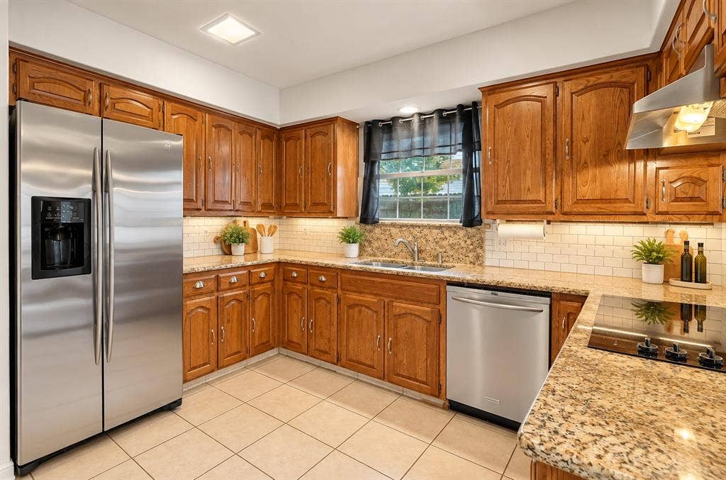 Kitchen featuring wood cabinetry, stone countertops, a subway tile backsplash, stainless steel appliances, and a double-basin sink