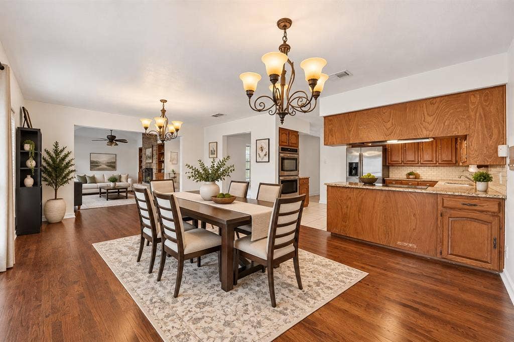 Dining area featuring wood-finish flooring, two decorative chandeliers, natural-finish wood cabinetry, and a stone-surface countertop