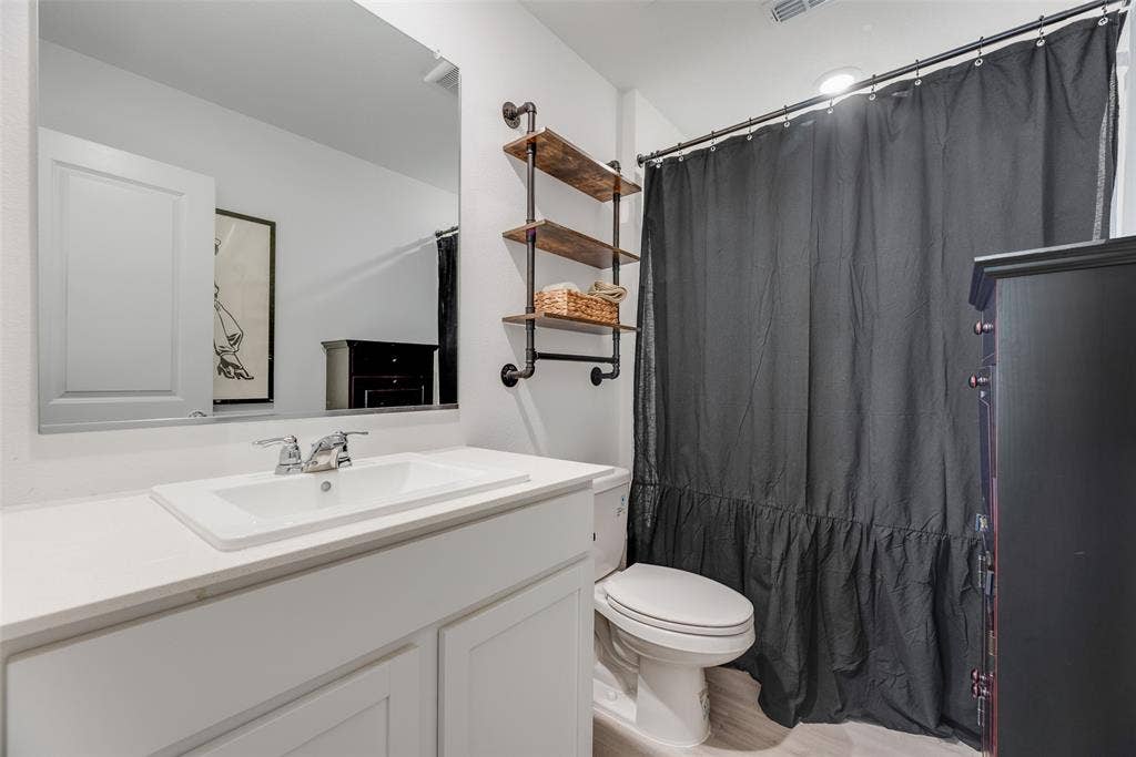6742 Highlands Street, Princeton, TX 75407 Bathroom featuring a white vanity with a rectangular drop-in sink, chrome hardware, a large frameless wall mirror, and industrial-style shelving with wood-finish tiered surfaces