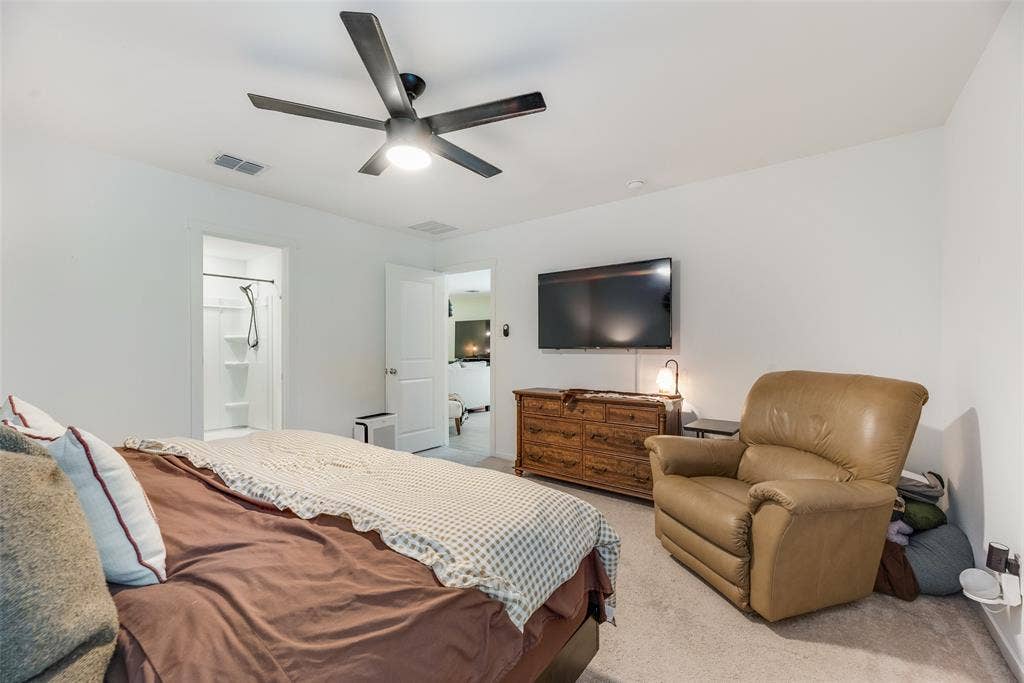 6742 Highlands Street, Princeton, TX 75407 Spacious room featuring neutral carpeting, a central ceiling fan with integrated lighting, and a doorway entry to an en suite bathroom with a shower enclosure