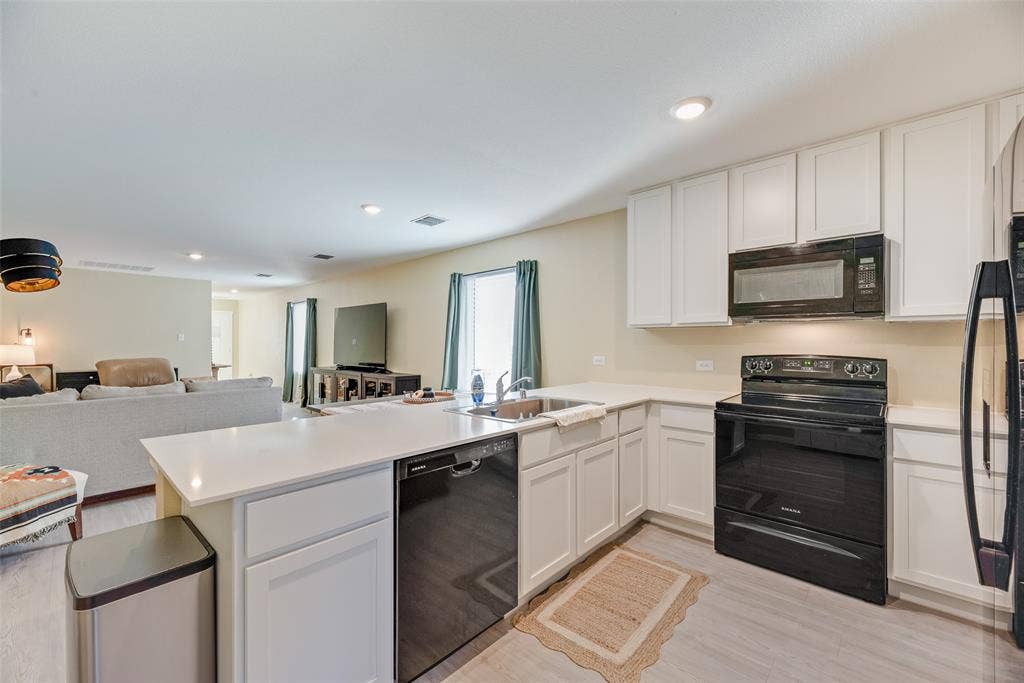 6742 Highlands Street, Princeton, TX 75407 Kitchen featuring white cabinetry, solid-surface countertops, black appliances, a stainless steel sink, and light-tone wood-finish flooring