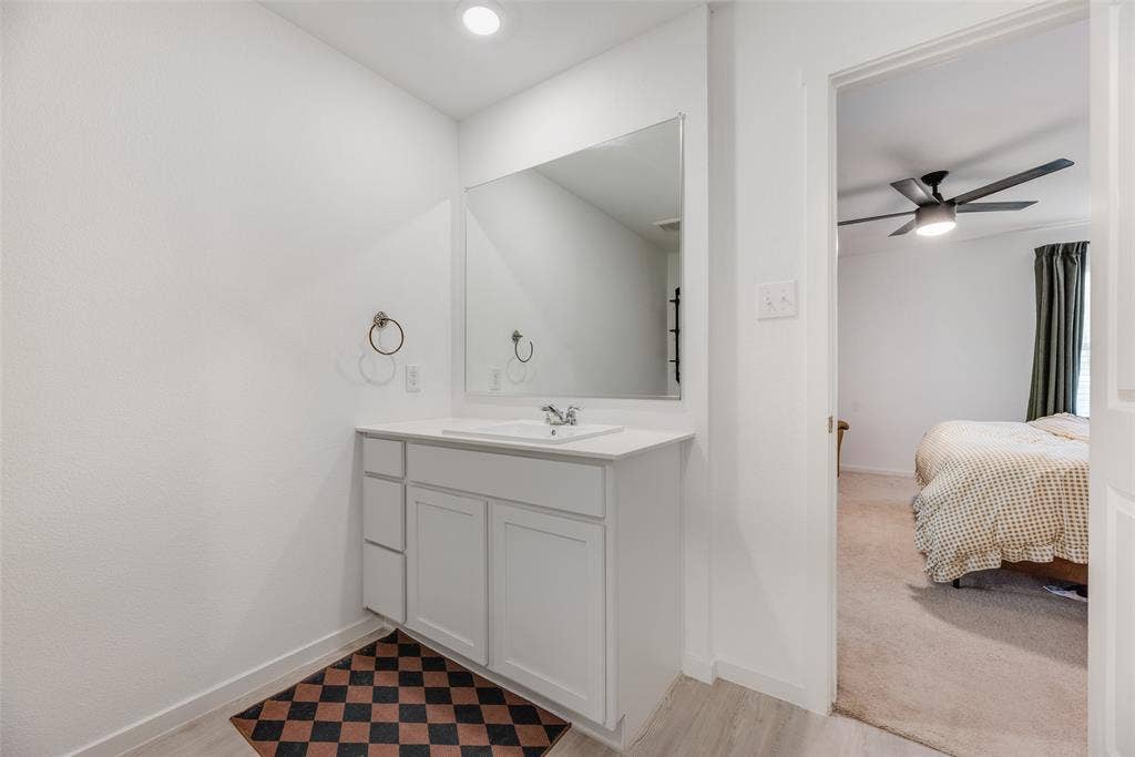 6742 Highlands Street, Princeton, TX 75407 Bathroom vanity featuring white shaker-style cabinetry, a solid surface countertop with an integrated basin, a large wall-mounted mirror, and polished chrome hardware