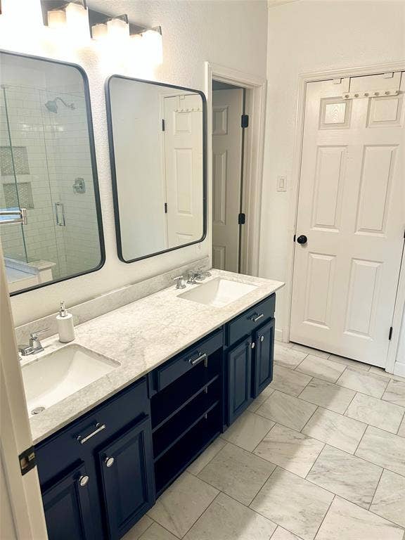 4327 Chasemoor Place, Frisco, TX 75035 Dual vanity featuring navy blue shaker-style cabinetry, light-toned stone-finish countertops, undermount sinks, and rectangular mirrors with black frames, complemented by white tile flooring