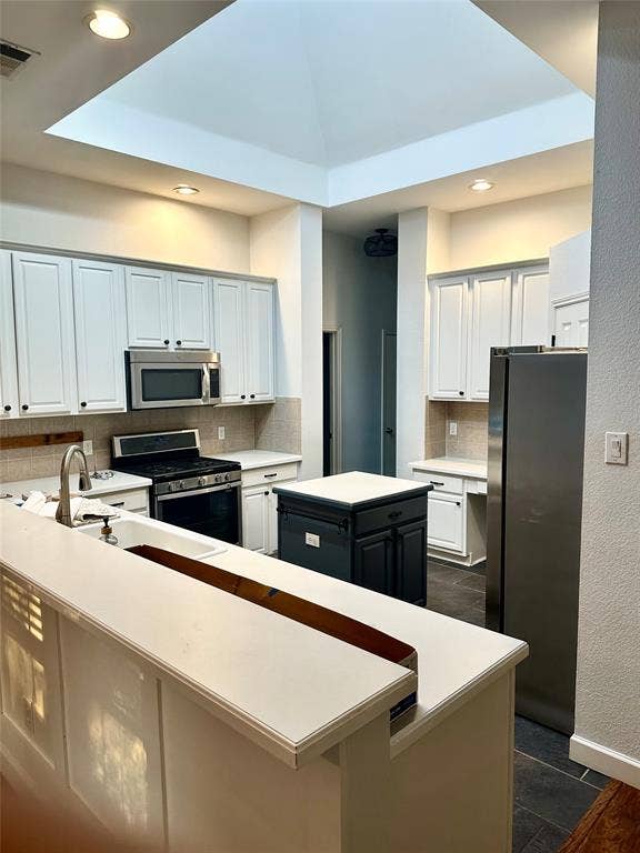 4327 Chasemoor Place, Frisco, TX 75035 Kitchen featuring a central pyramid skylight, white shaker-style cabinetry, stainless steel appliances, a dark-toned center island, and solid-surface countertops