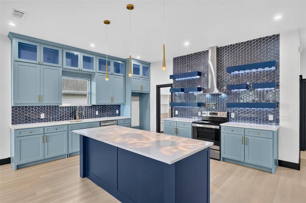 601 Melody Circle, Kaufman, TX 75142 Kitchen featuring light blue cabinetry, center island with quartz countertop, hexagonal tile backsplash, stainless steel range with chimney-style hood, and tiered floating shelving with integrated lighting