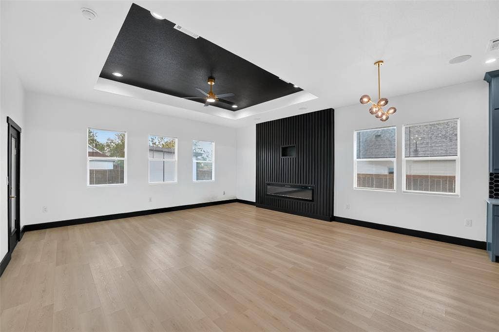 601 Melody Circle, Kaufman, TX 75142 Tray ceiling with black recessed lighting, wood-finish flooring, vertical slat feature wall, built-in electric fireplace, and multi-light brass fixture